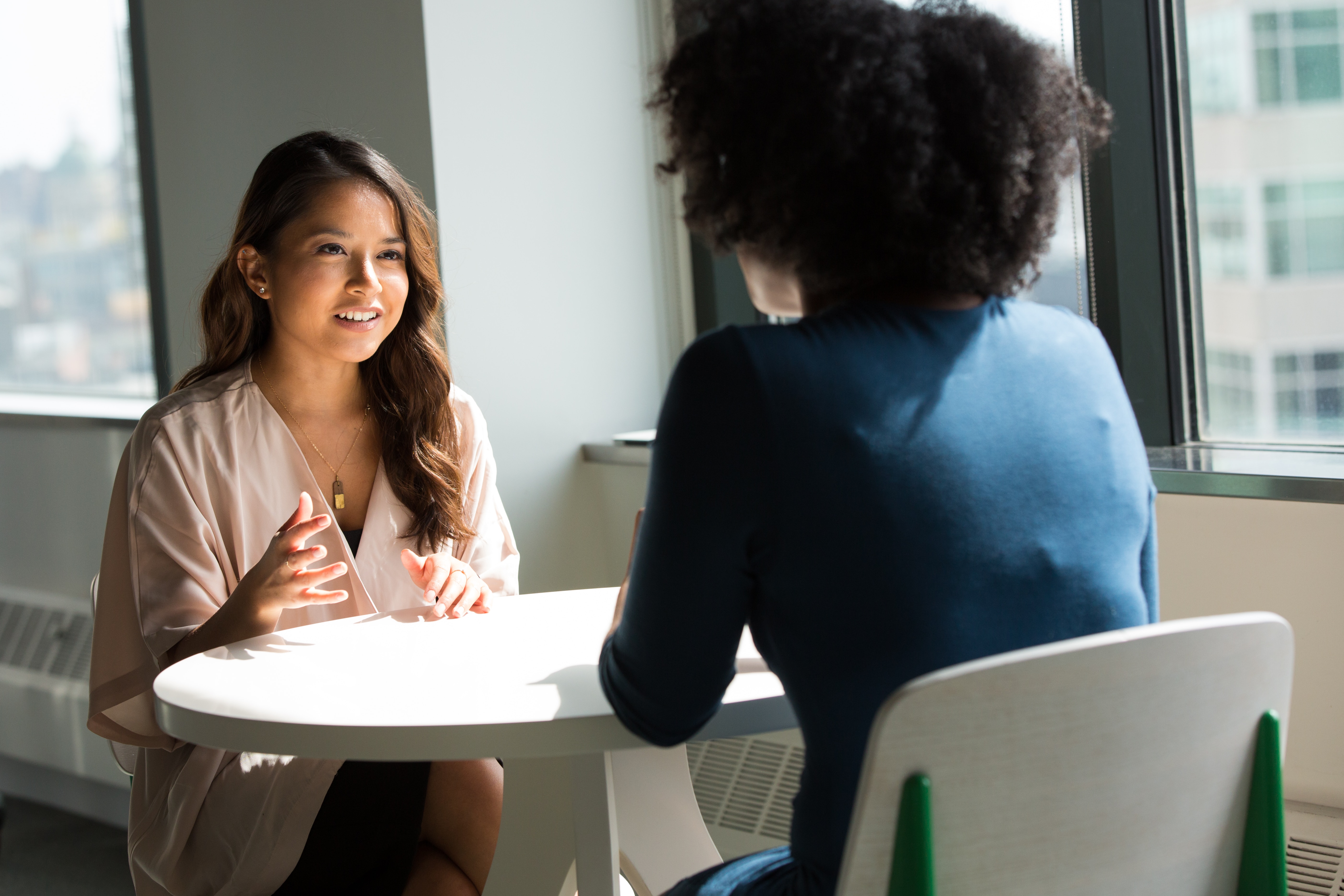 two women meeting at a table, one facing the camera and one with back to the camera