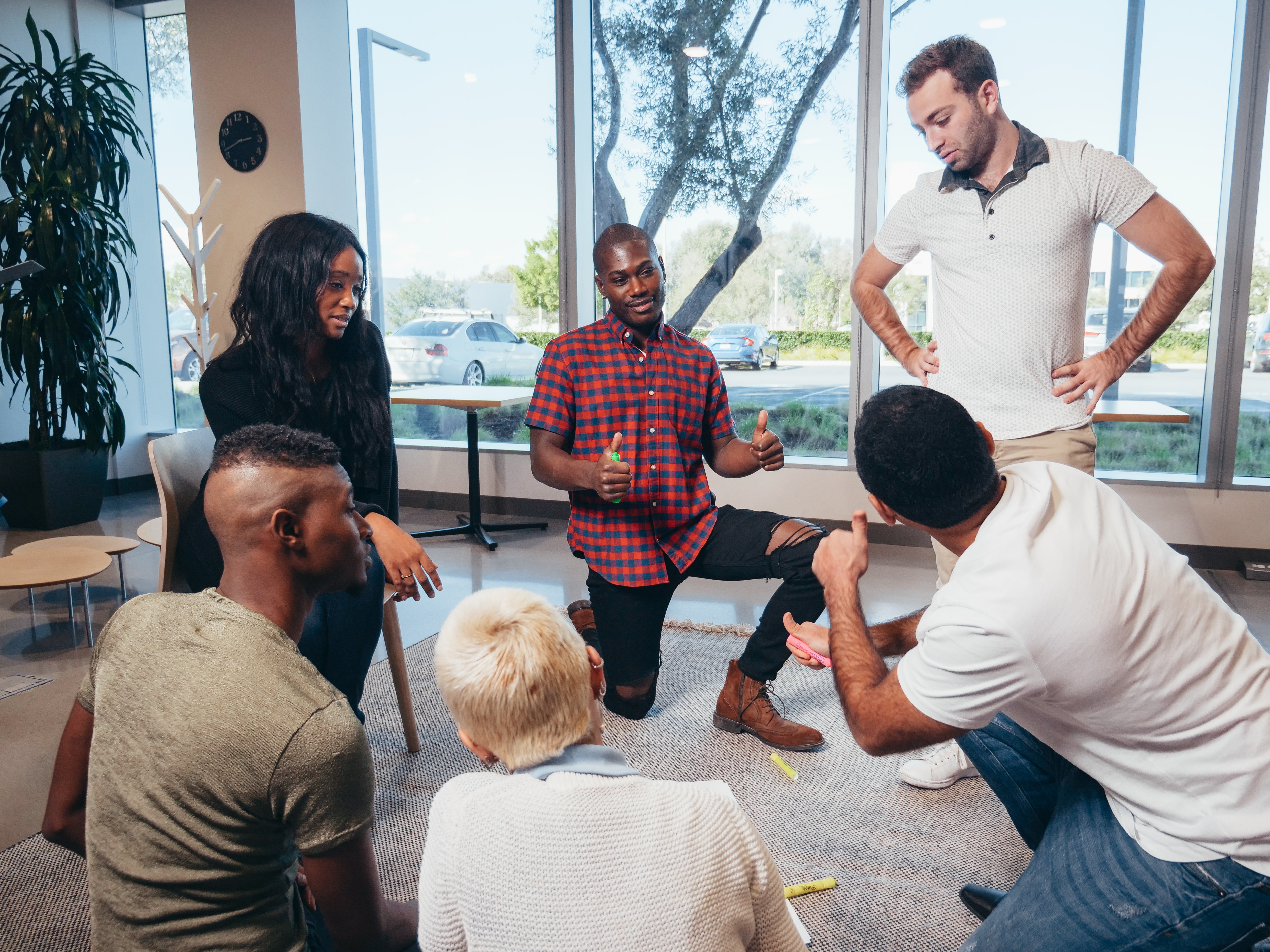 group of adults in a circle talking with one another, some sitting on the ground, some kneeling, one man standing